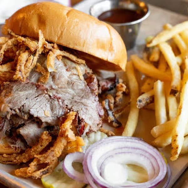 A roast beef sandwich with crispy fried onions, fries, and red onion slices on a tray.