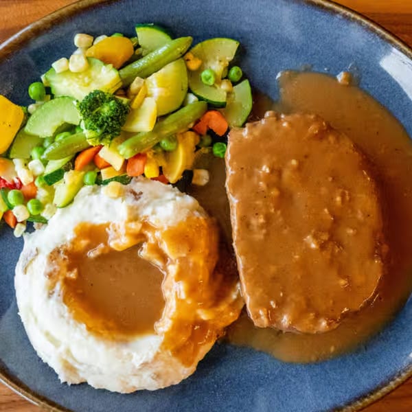 Castle Cafe's Salisbury steak with gravy, mashed potatoes, and mixed vegetables on a blue plate.