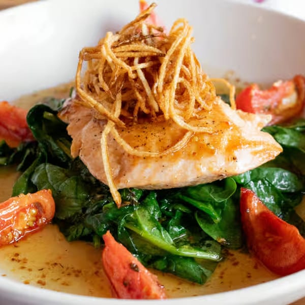 Pan-seared salmon topped with crispy fried onions, served over spinach with tomato wedges.