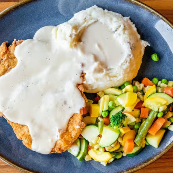Chicken fried steak with gravy, mashed potatoes, and mixed vegetables on a blue plate.